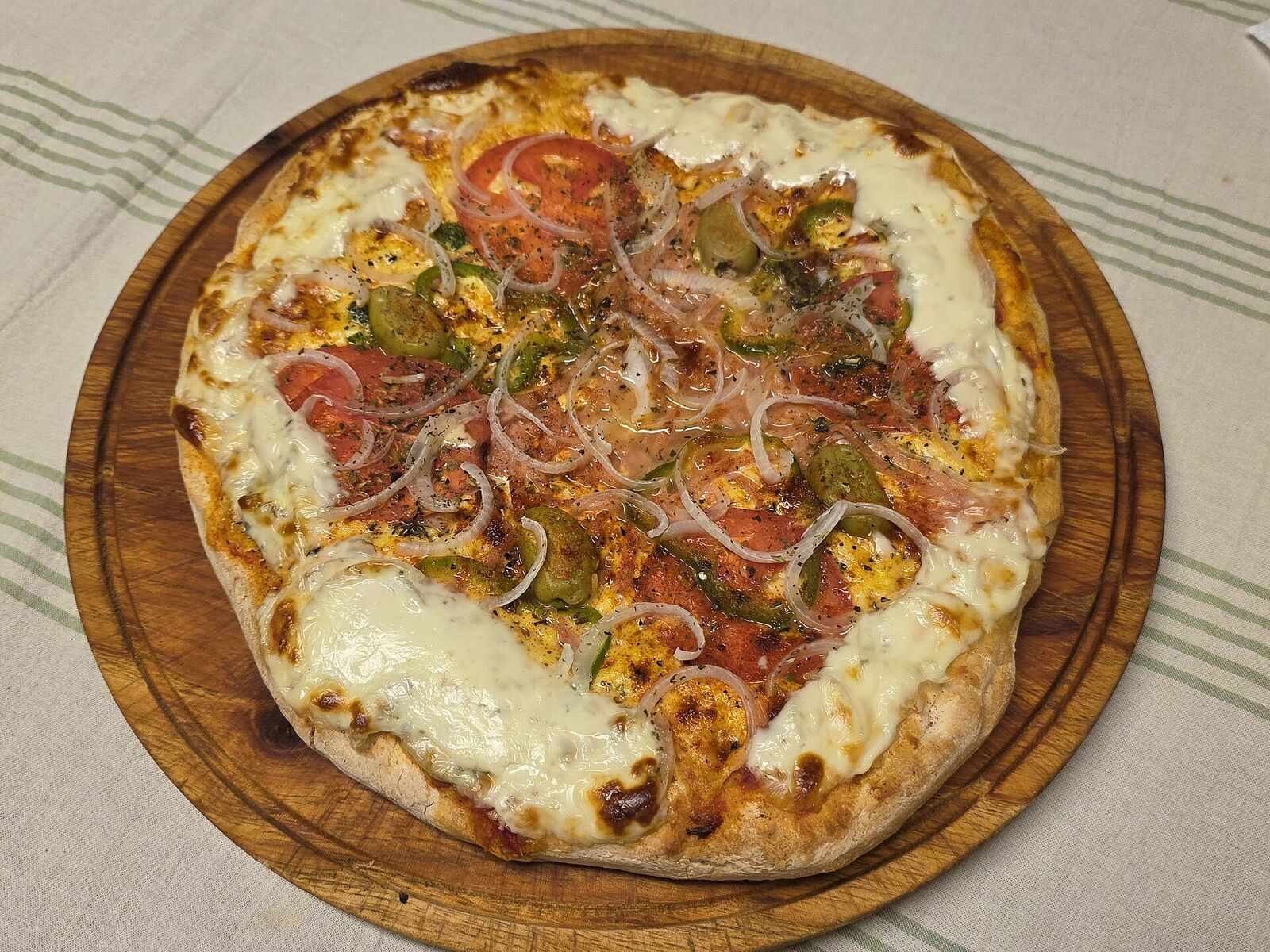 Whole pizza on a round wooden board seen from above
